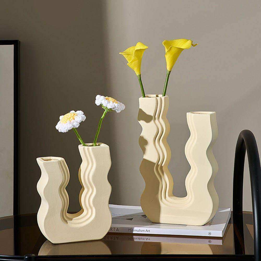 Cream-colored ceramic wavy wonder vase holding yellow calla lilies and white daisies with sculptural design