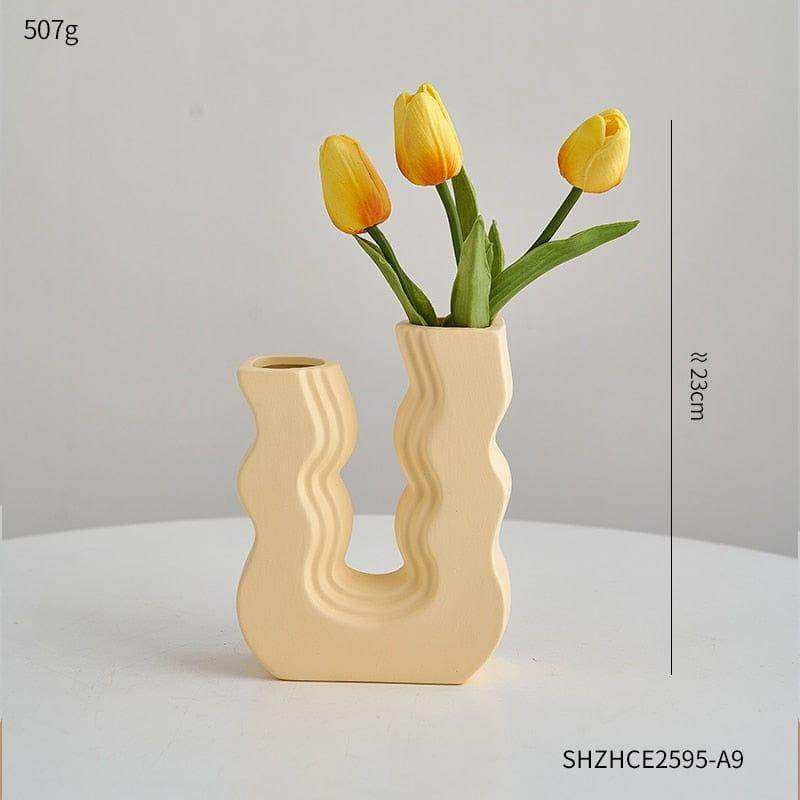 Cream-colored ceramic wavy wonder vase with u-shaped design holding three yellow tulips