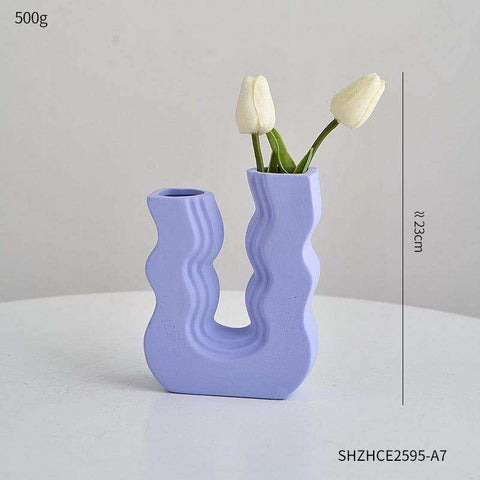 A lavender ceramic wavy wonder vase with a u shaped design holding two white tulips