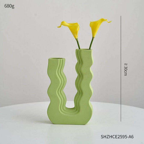 A light green ceramic wavy wonder vase with a u-shaped design and two openings holding yellow calla lilies