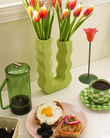 A pair of vibrant green wavy ceramic vases called wavy wonder vase holding red and yellow tulips