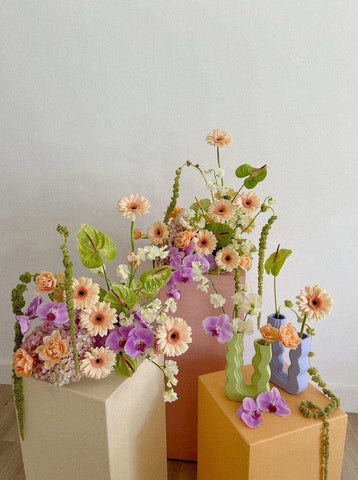 Pastel-colored ceramic wavy wonder vases with modern designs holding peach purple and white flower arrangements