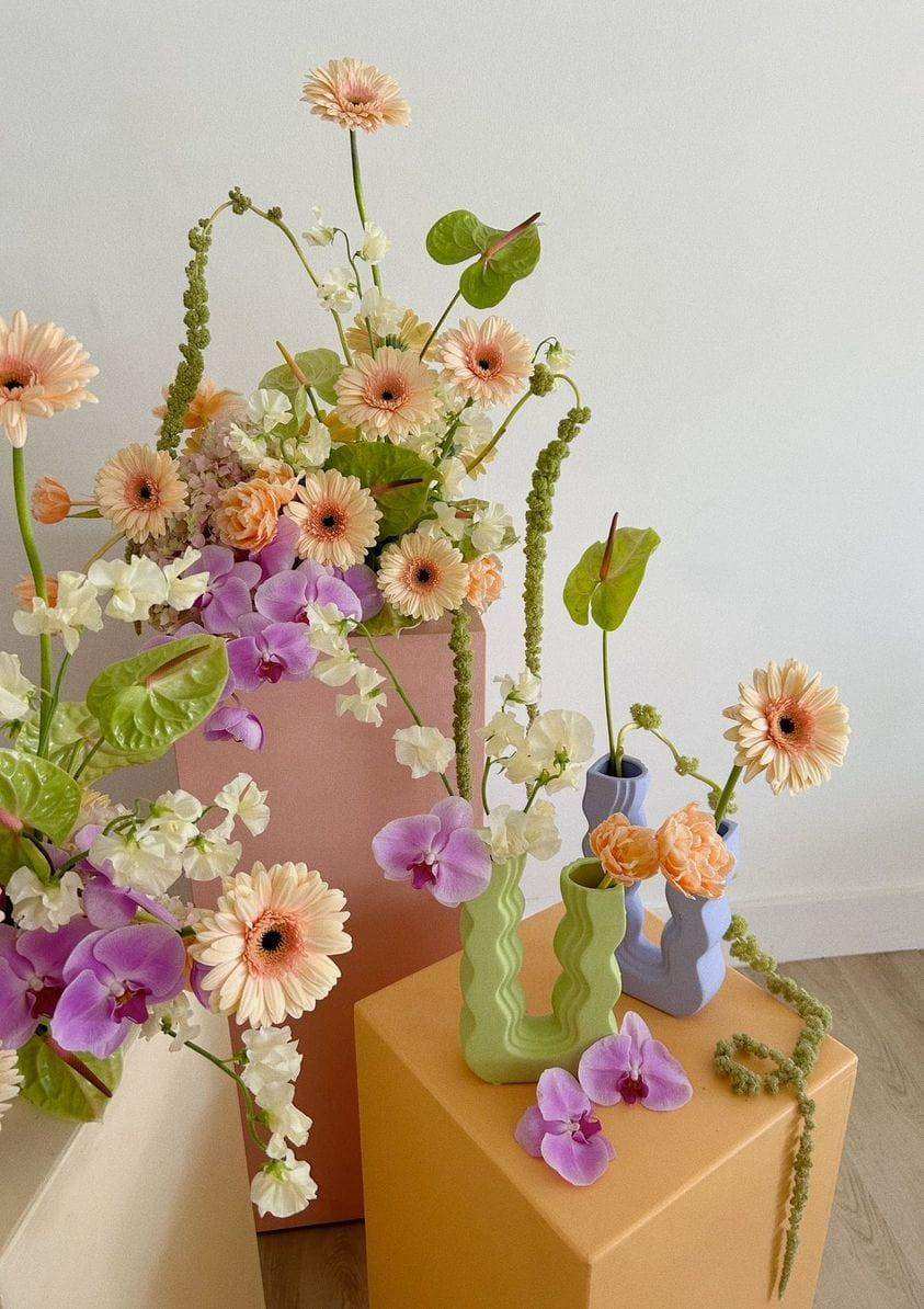 Pastel-colored ceramic wavy wonder vase with modern wavy design holding gerbera daisies and purple orchids