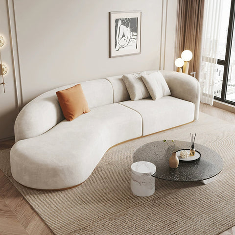 Cream-colored plush velvet welby three seater curved sofa with one orange throw pillow in a modern design