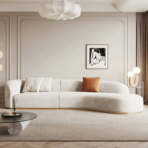 Cream-colored welby three seater curved sofa with soft velvet texture and light wood base for stylish seating