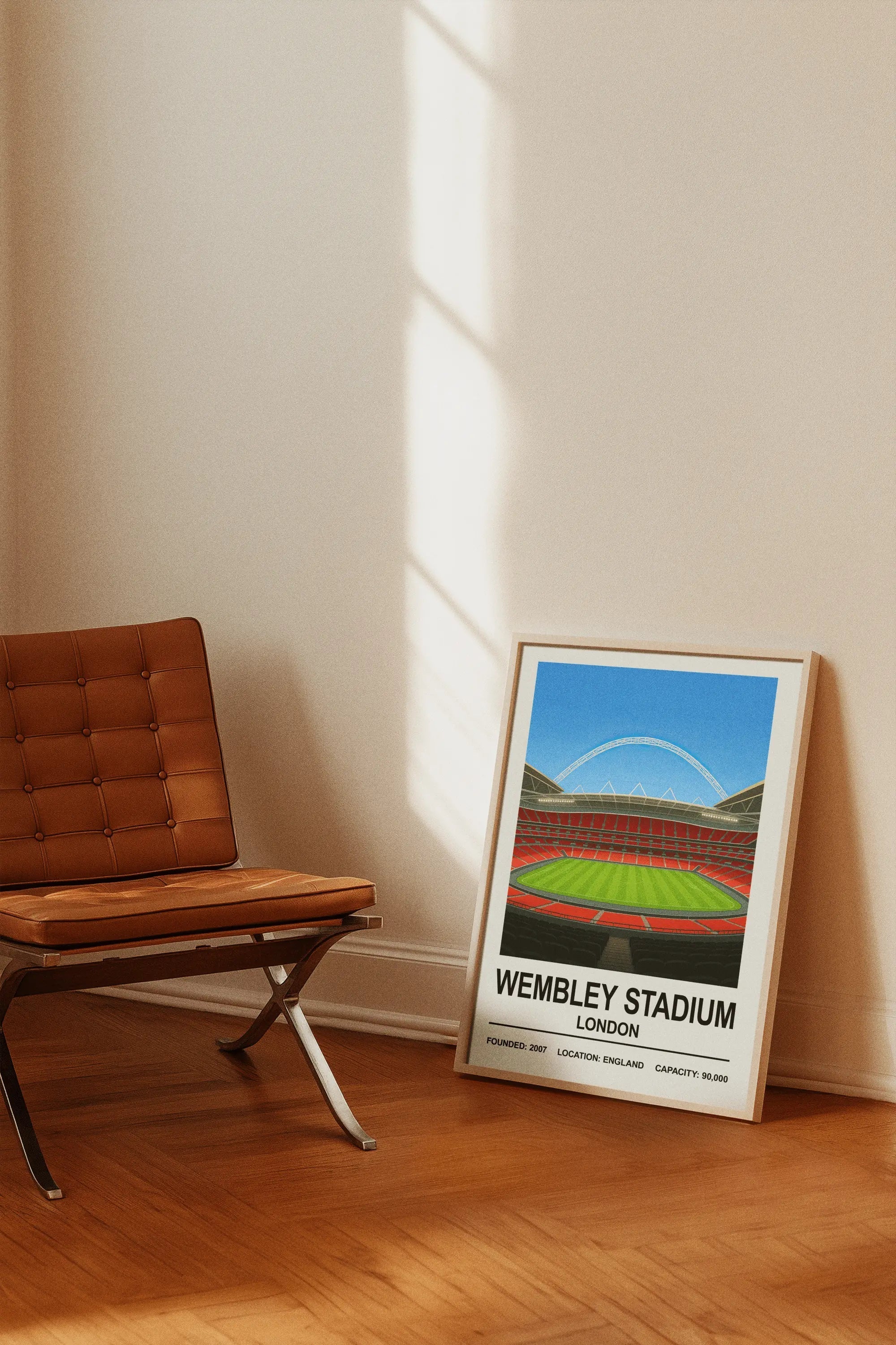 A framed wembley stadium poster showing a vibrant illustration of the stadium with red seats and green grass under blue sky