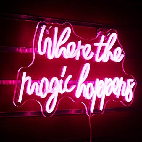 A glowing pink led neon sign with the phrase where the magic happens in cursive for bedroom wedding decor