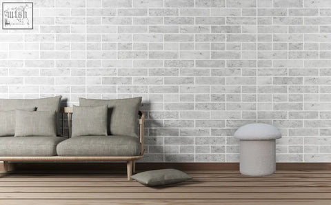Gray upholstered sofa with wooden legs and matching pillows next to a white boucle mushroom footstool against white brick wall