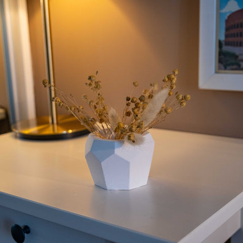 White concrete bee-home pot with geometric design holding dried golden flowers and fluffy pampas grass