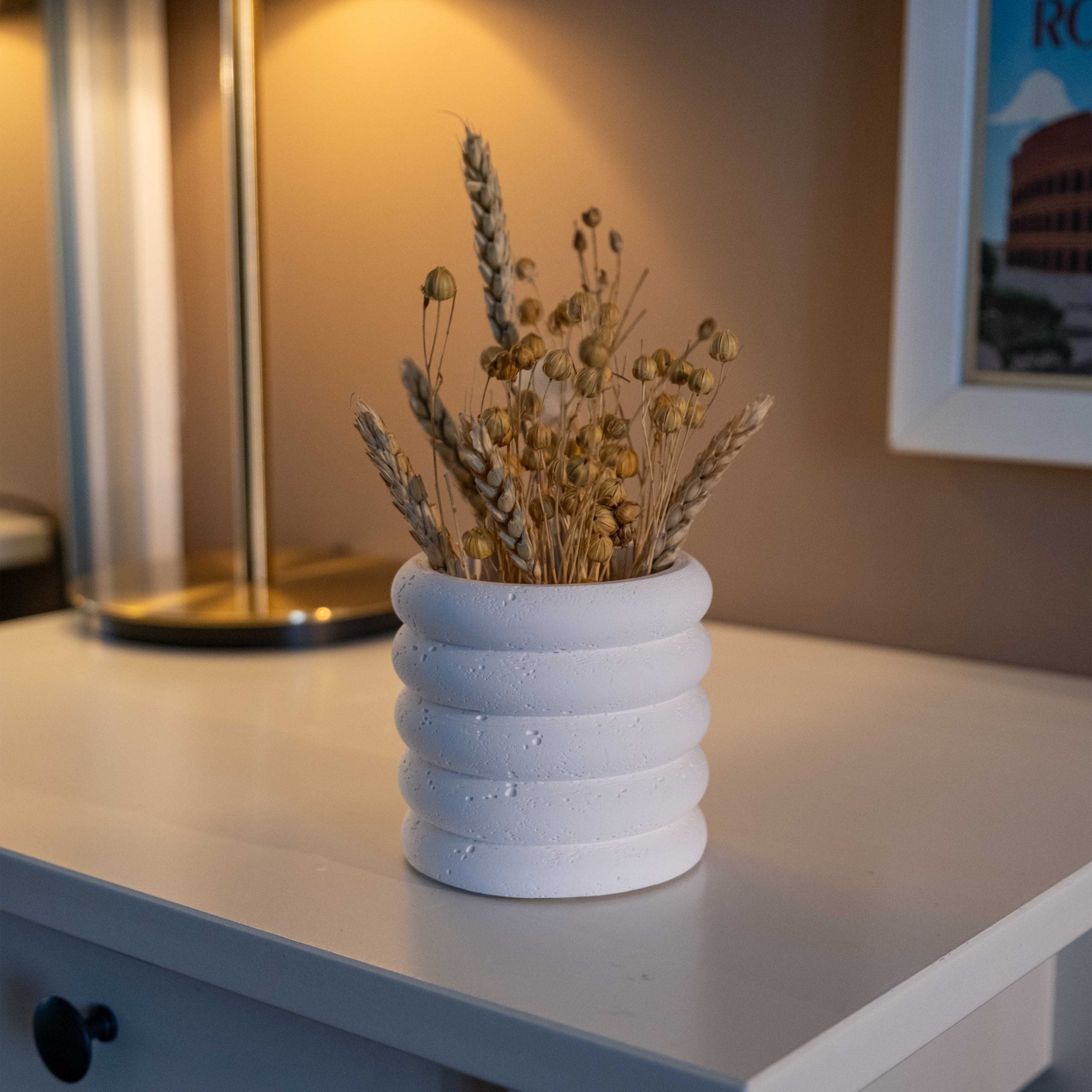 White concrete fold pot with concentric ridged bands holding dried wheat and golden seed pods in white concrete design