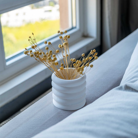 White concrete fold pot with ribbed texture holding dried golden flowers in a white concrete ceramic vase