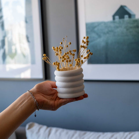 White concrete fold pot with stacked ribbed design holding dried golden flowers in a white concrete vase