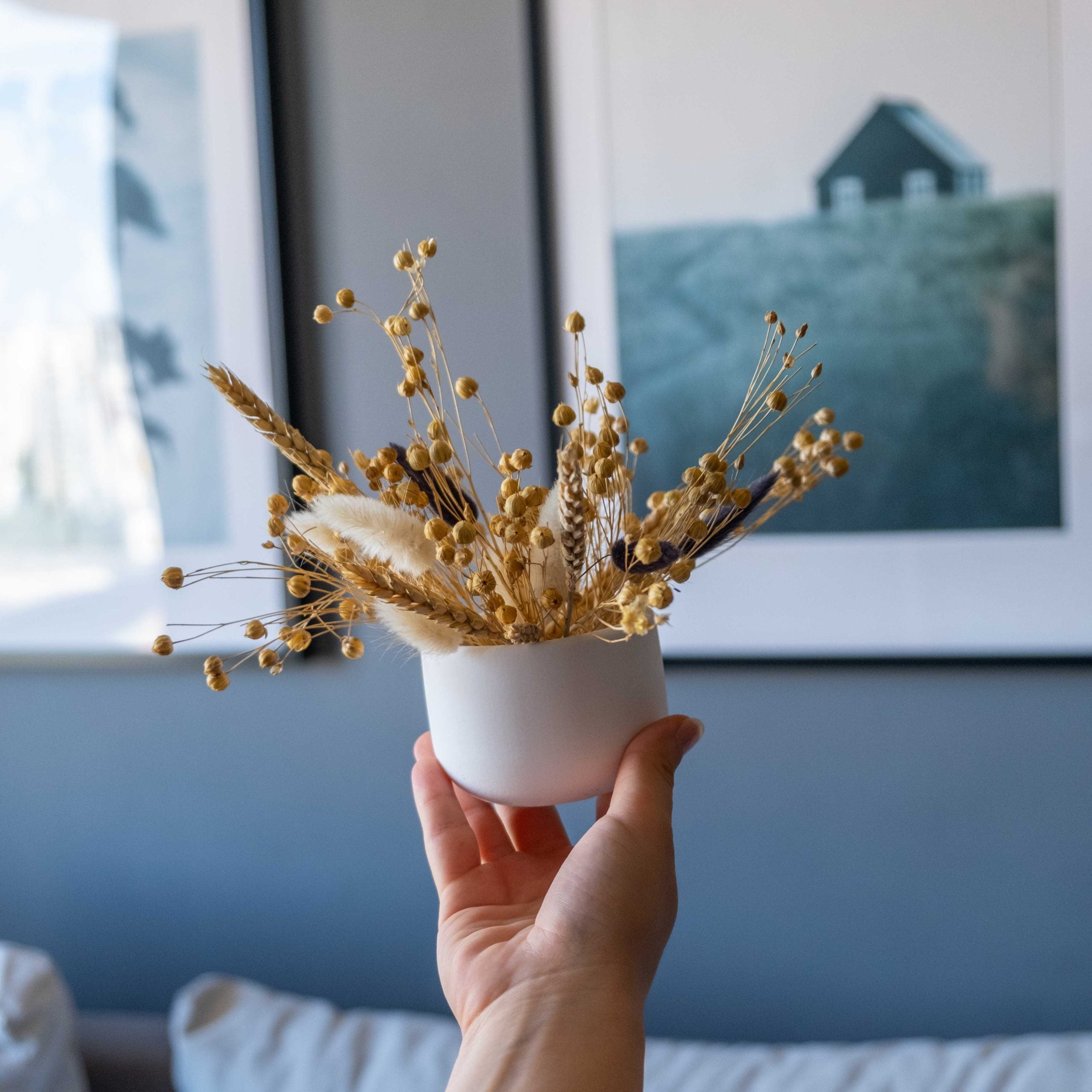 A hand holds a white concrete pine pot with dried golden wheat and seed pods for rustic decor