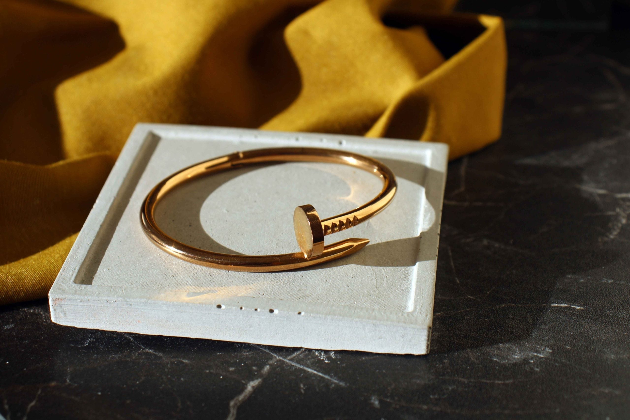 White concrete square jewellery holder with gold-tone nail-shaped bracelet featuring polished finish and handmade concrete design