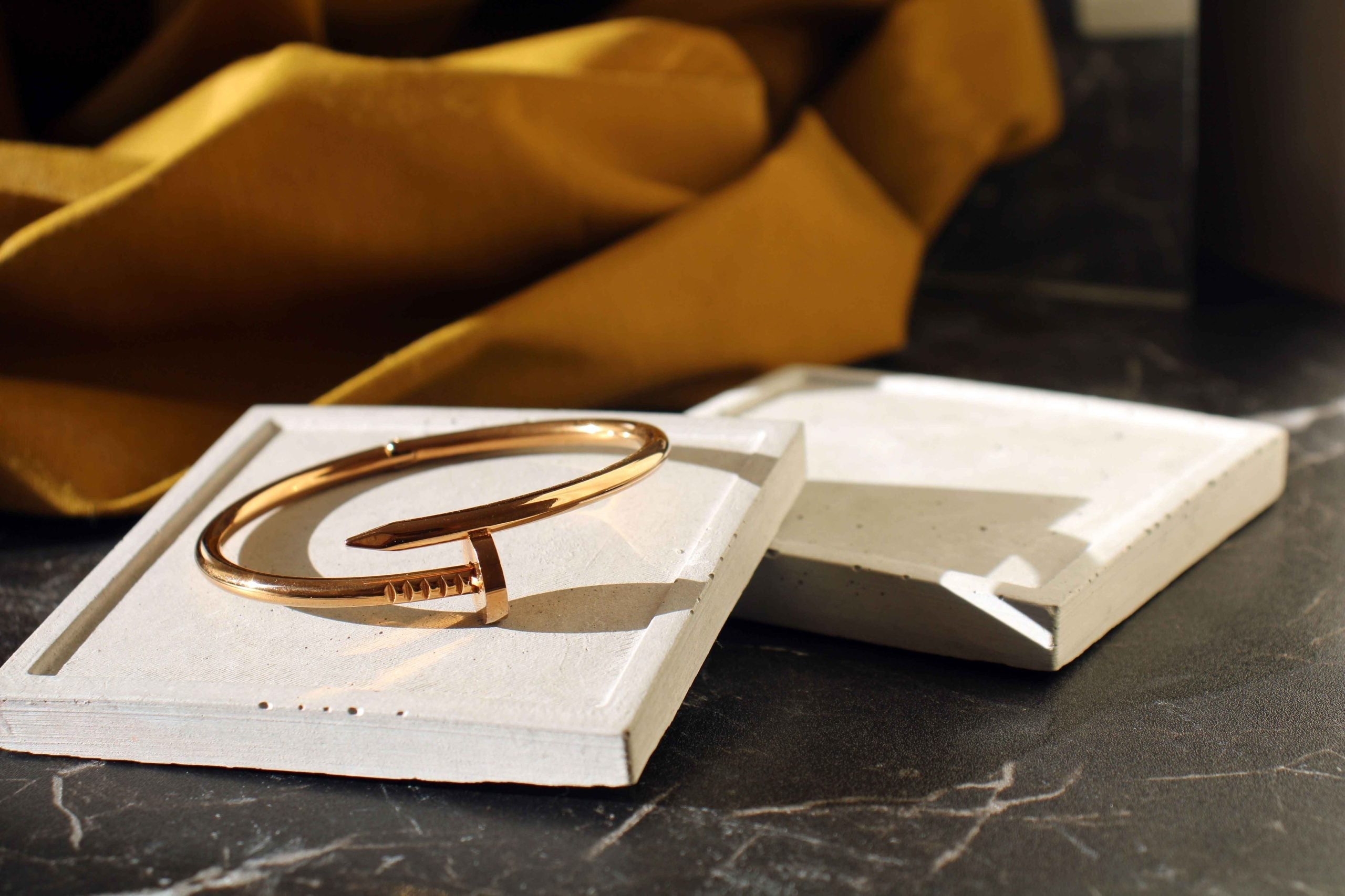 A sleek rose gold nail-inspired cuff bracelet resting on a high quality handmade concrete white concrete square jewellery holder great gift idea