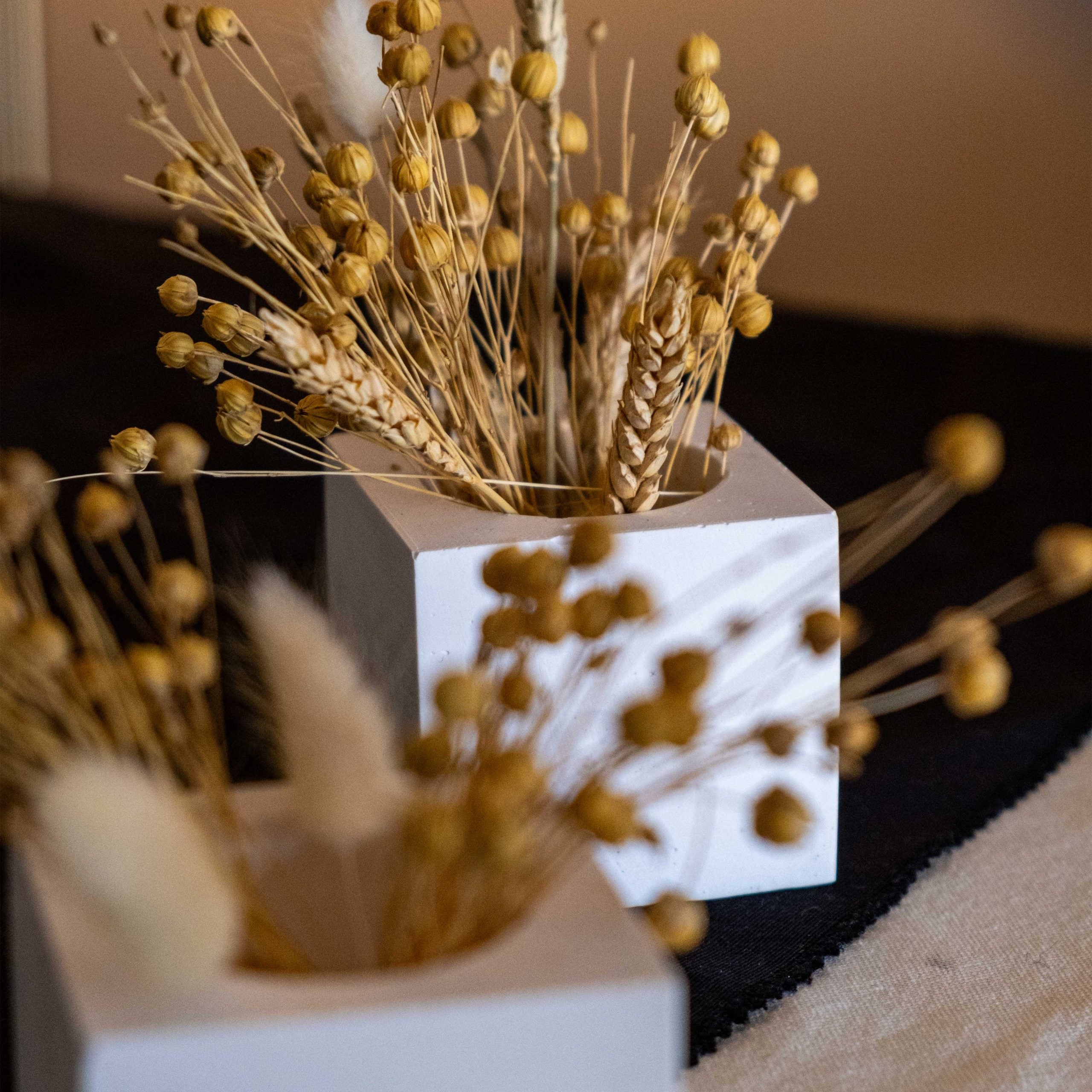 White concrete square pot with white marble texture holding dried golden seed pods and wheat stalks