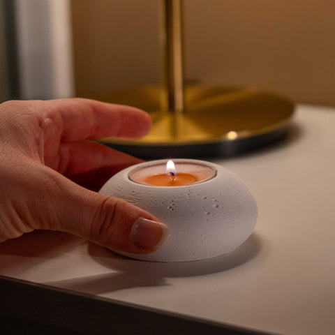 White concrete tealight holder with textured surface and lit orange tea light inside from the double set