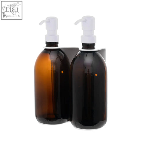 White wall-mounted soap dispenser with two amber glass bottles and white pump dispensers on a dark gray bracket