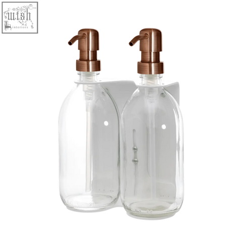 White double wall mounted soap dispenser with clear glass bottles and rose gold pumps on a white wall-mounted bracket