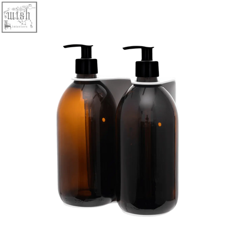 Two amber and dark brown glass bottles with black pumps on a white wall-mounted soap dispenser holder
