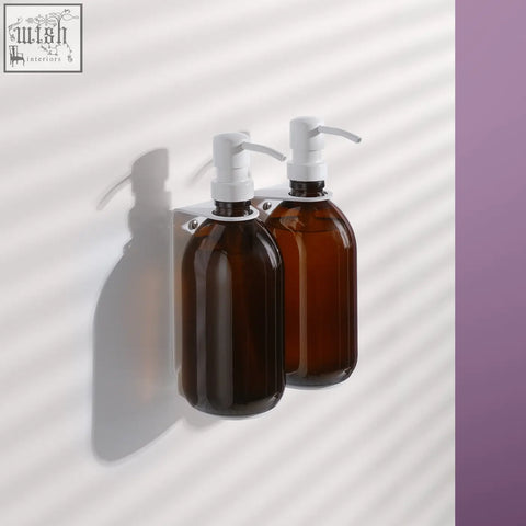 Two amber glass bottles with white pump soap dispensers on a white wall-mounted bracket for easy use