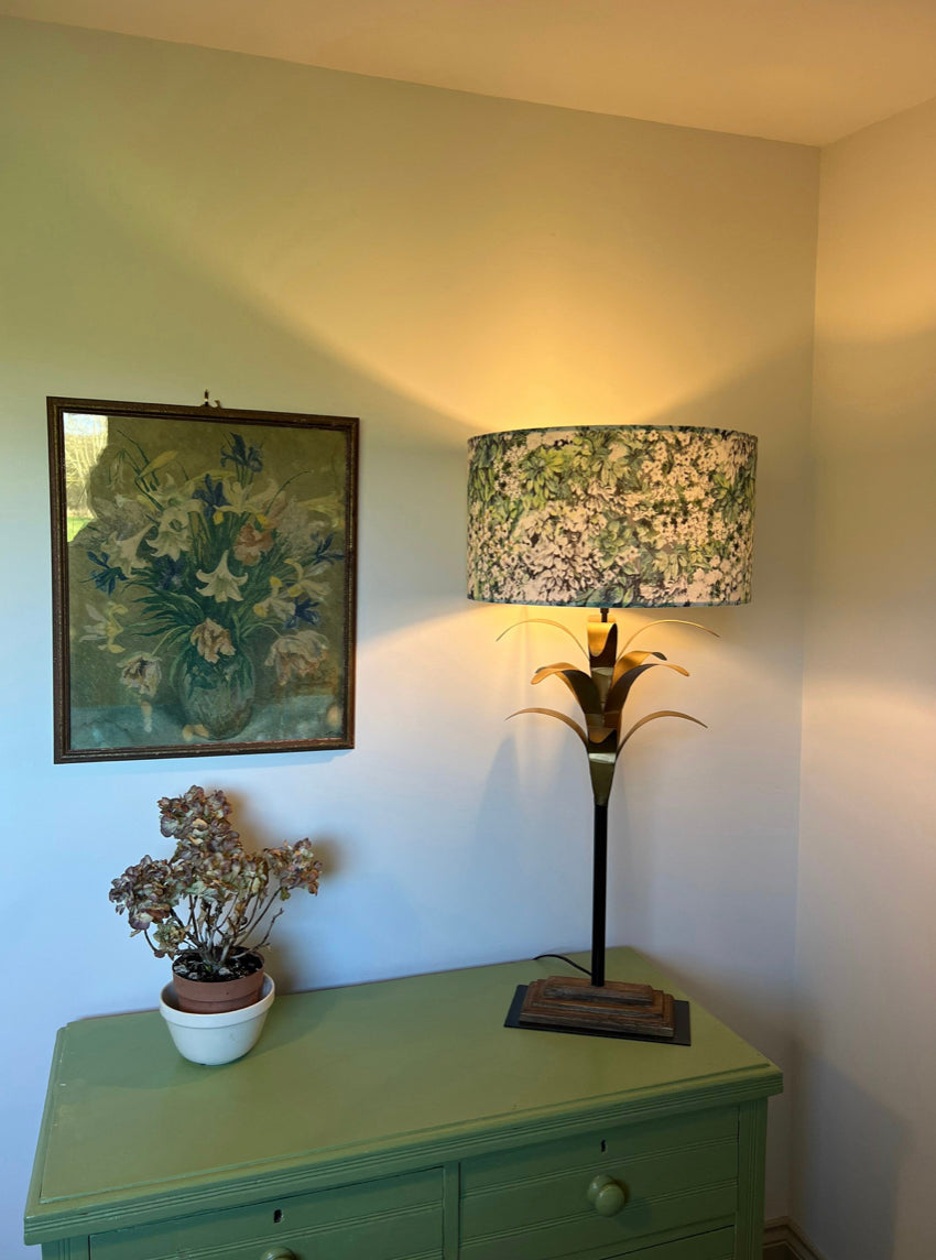 A vintage-style table lamp with a black metal palm frond base and a white flowers velvet drum ceiling shade fitting sits 3-4cm