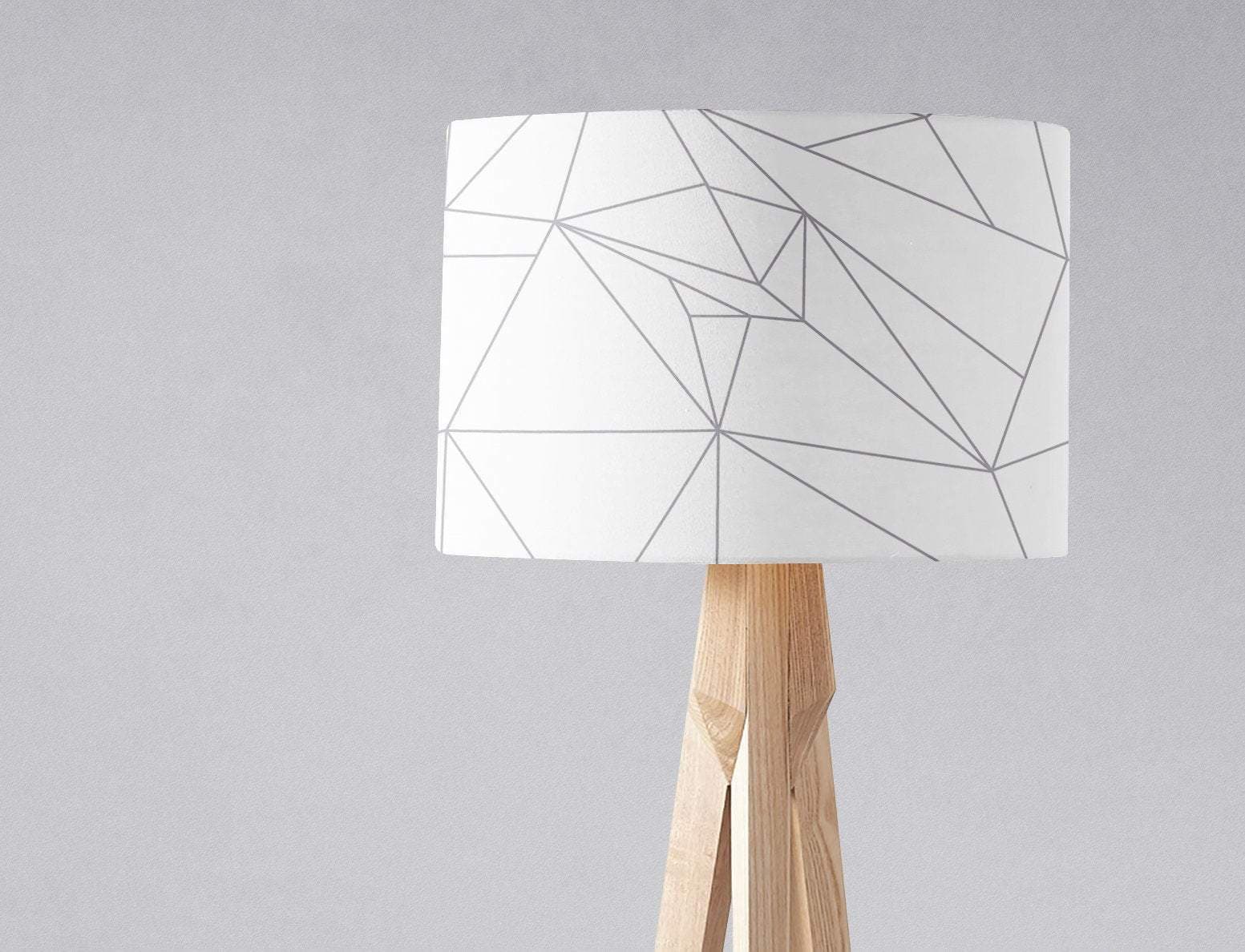 White table lamp shade with gray lines geometric design on a light wood tripod base with inch diameter size