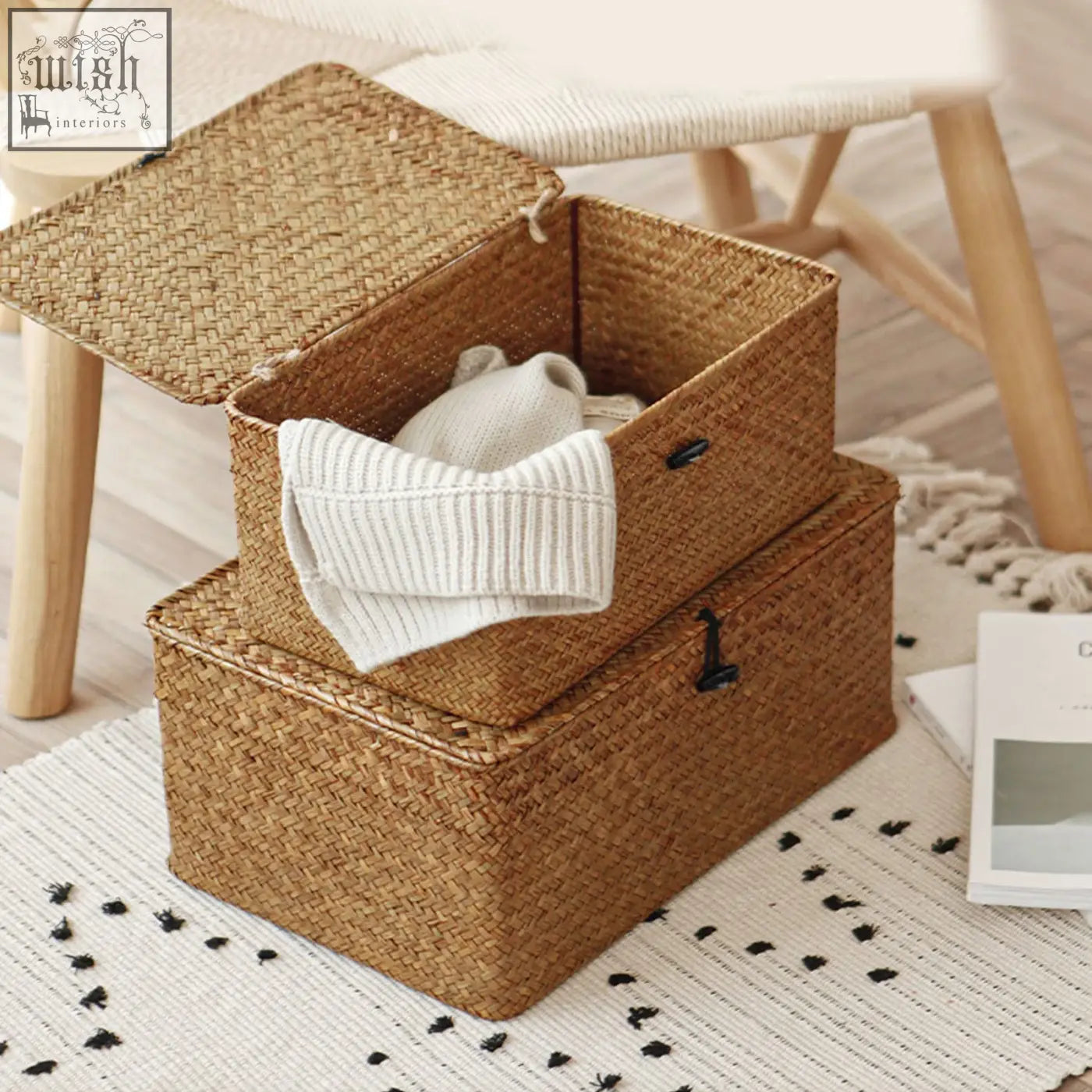 Natural woven seagrass storage baskets with black metal latches and hinged lids, one holding a white ribbed sweater