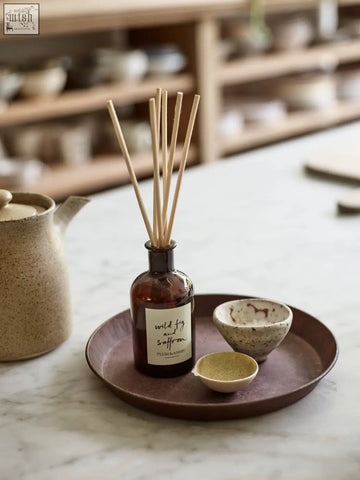 A dark amber glass wild fig and saffron diffuser with light brown wooden reeds for consistent fragrance throw using vegetable oil