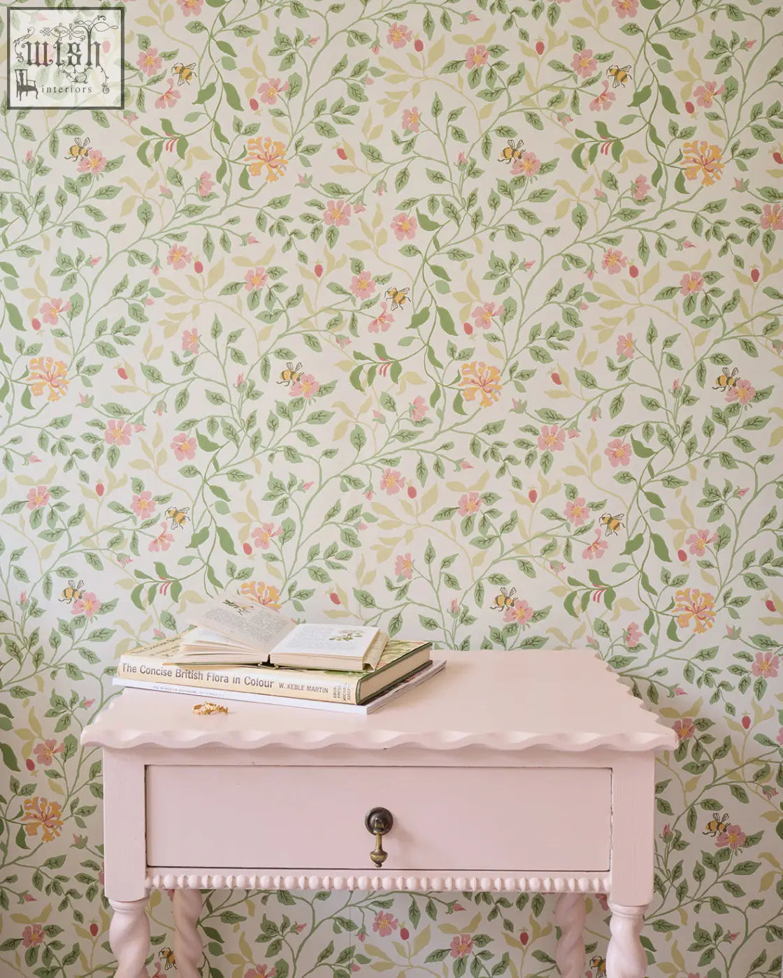 Pastel pink vintage side table with scalloped edges and ornate brass knob set against alex monroe wild rose wallpaper peridot