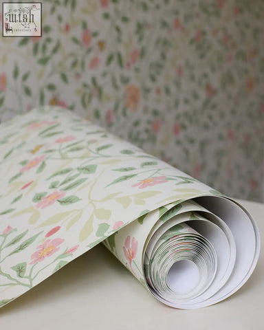 A roll of wild rose wallpaper by alex monroe with soft pink blossoms and green leaves on creamy off-white background