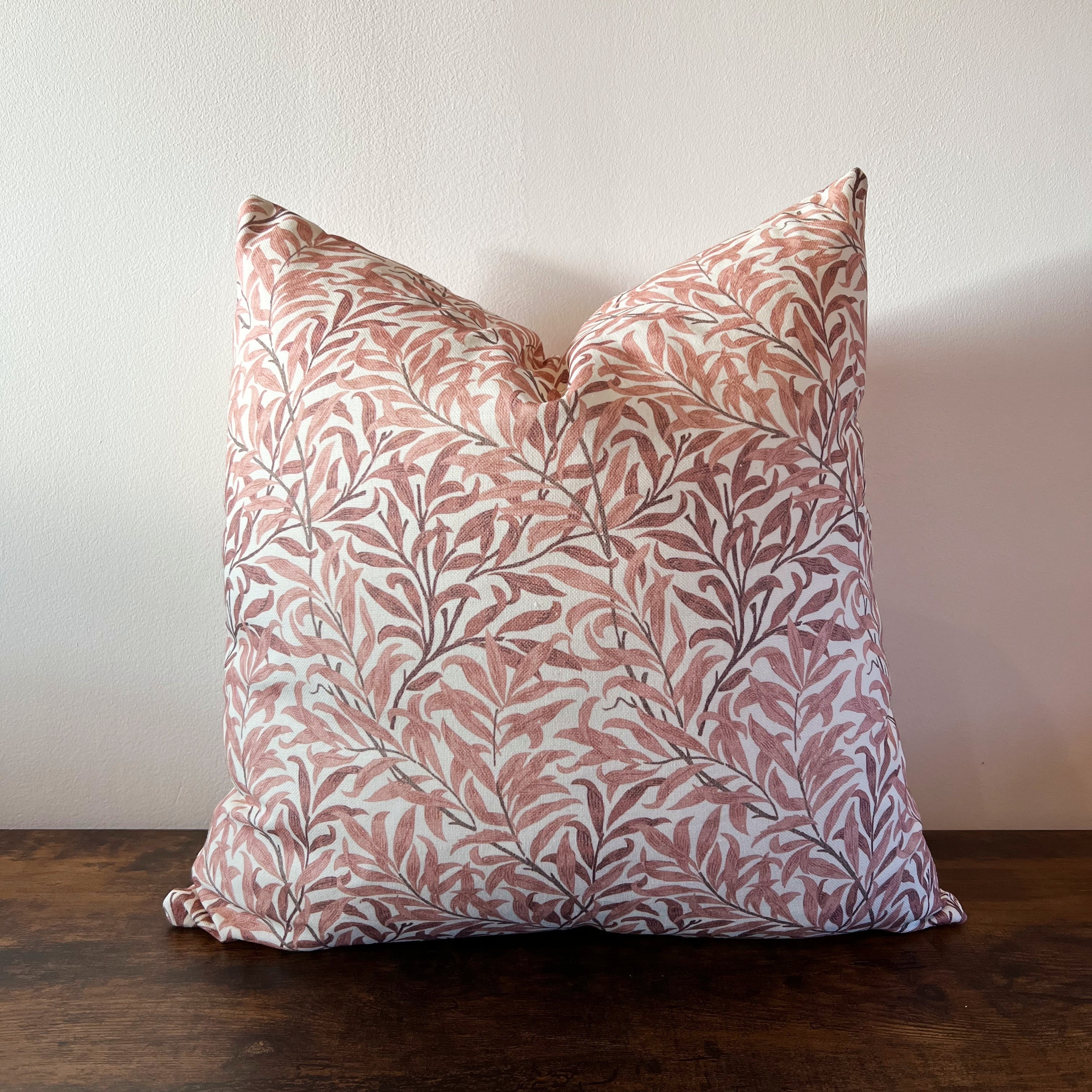 A william morris rust cotton cushion with rust willow leaves pattern in pink and gray on cream fabric