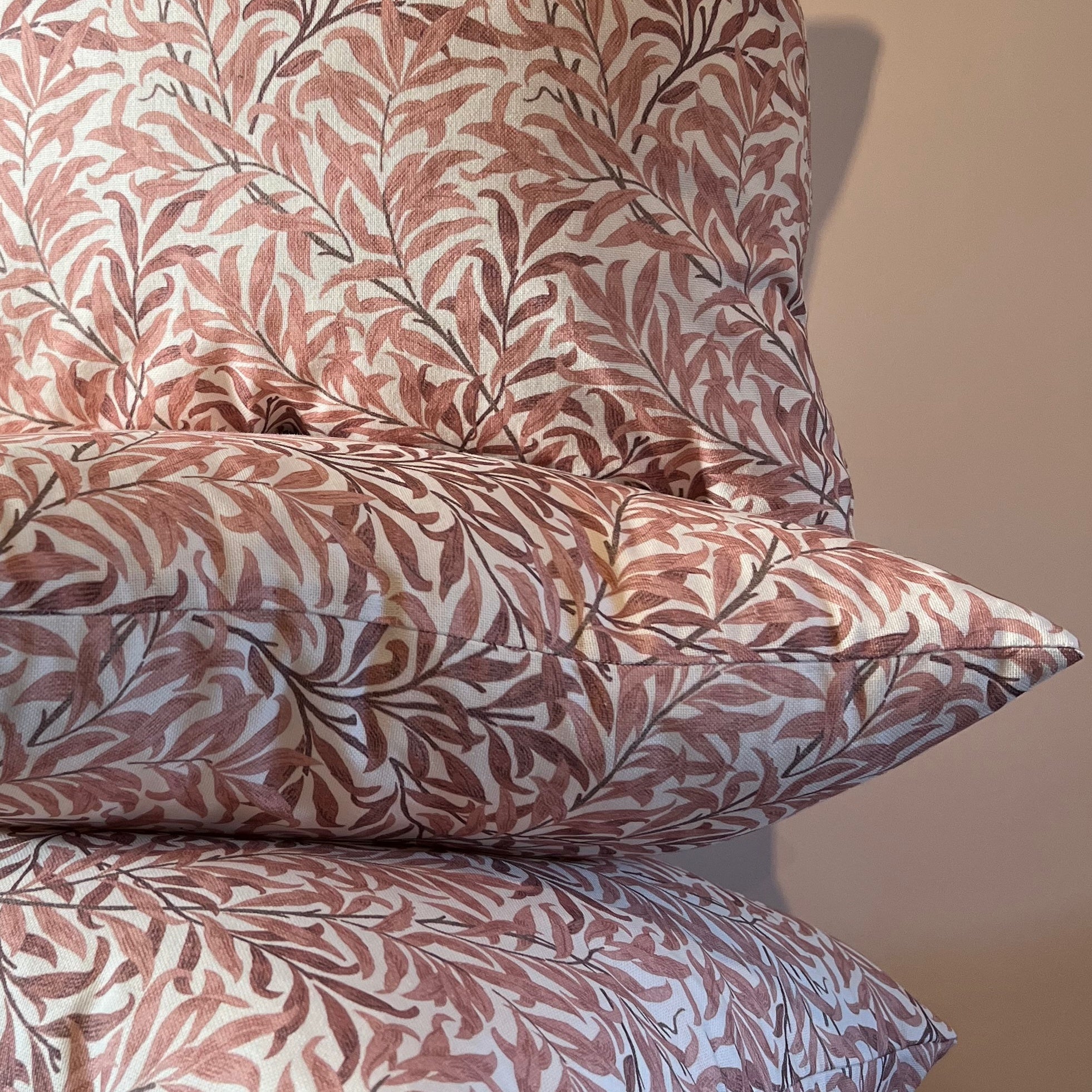 Stacked william morris rust willow leaves cotton cushions with muted rose and brown leaf pattern on cream fabric