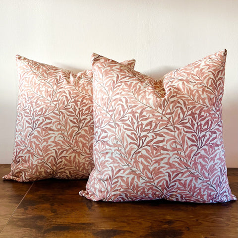Two william morris rust cotton cushions with rust willow leaves pattern in dusty rose on off-white background