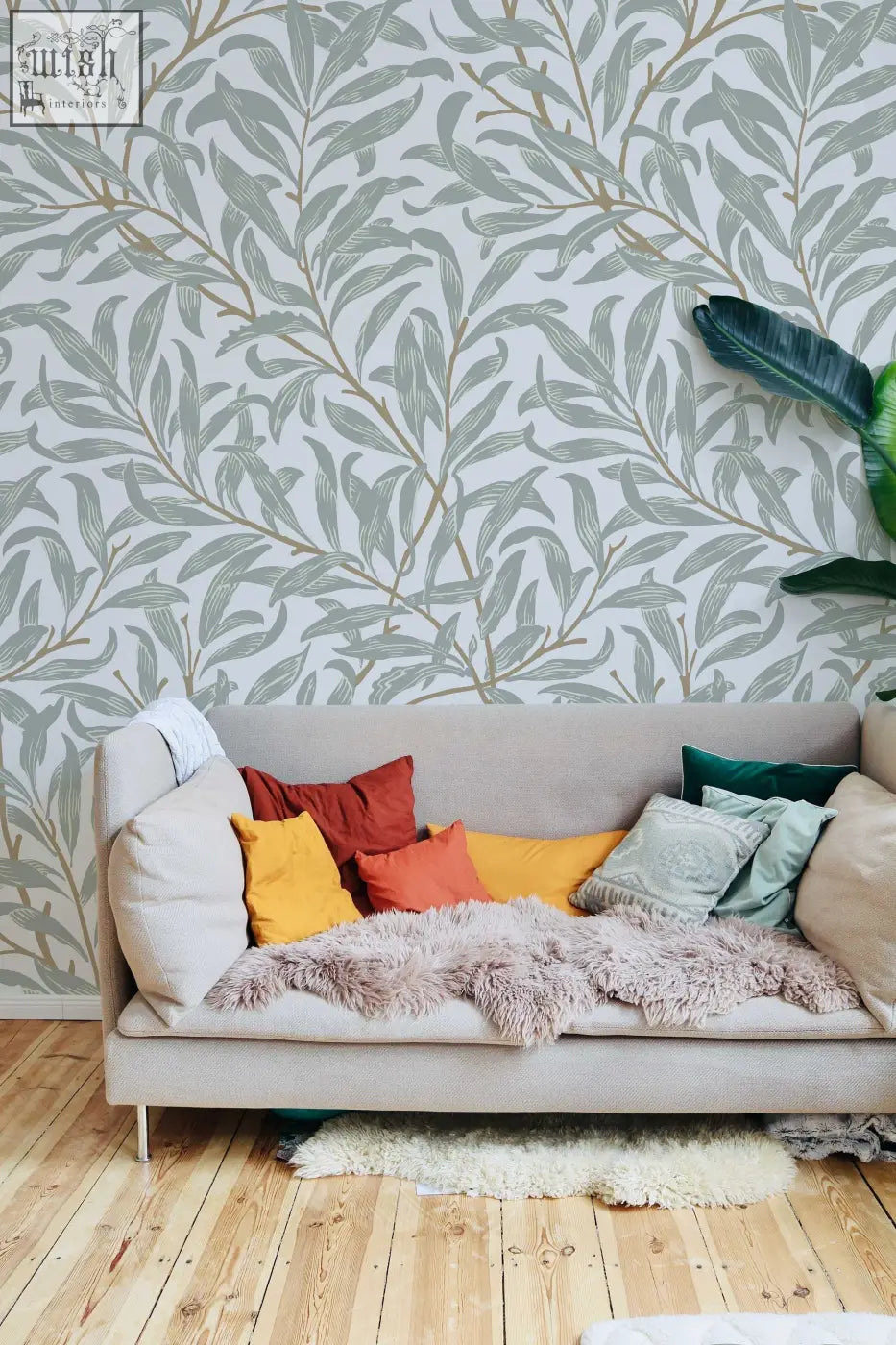 Beige upholstered sofa with colorful pillows and lavender blanket in a living space featuring willow bough william removable wallpaper