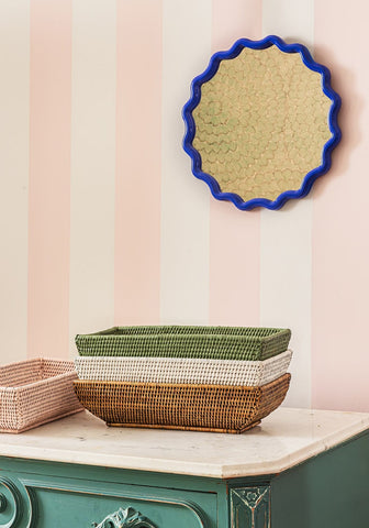 Stacked long rattan baskets in white, green, and brown woven tones sitting on a teal dresser