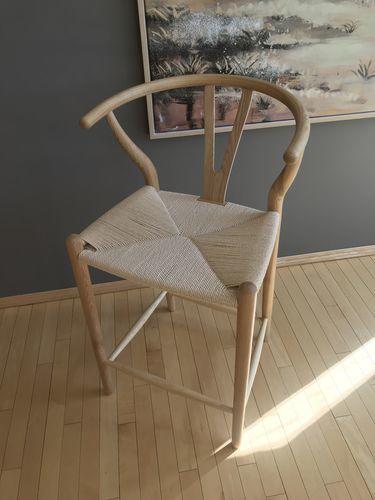 A light-colored wooden wishbone bar stool with woven seat and curved backrest in black ash finish for bar stools