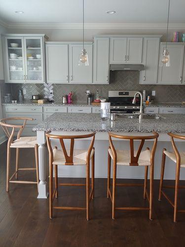Light gray kitchen cabinets with glass-paneled doors and granite countertop beside wishbone bar stool black ash bar stools