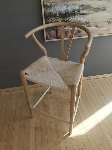 A light-colored wooden wishbone bar stool with a woven seat and distinctive curved backrest in walnut finish