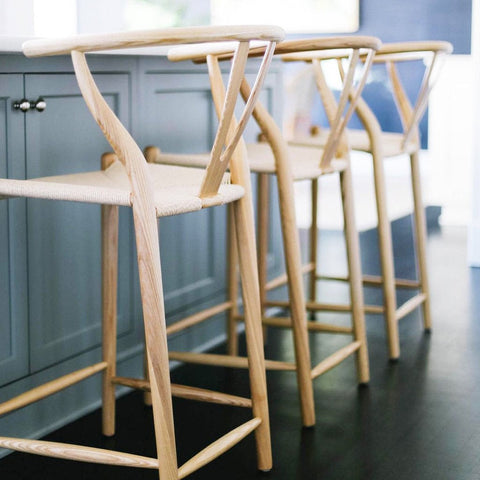 Light-colored wooden wishbone bar stool with y-shaped backrest and woven seat in walnut finish