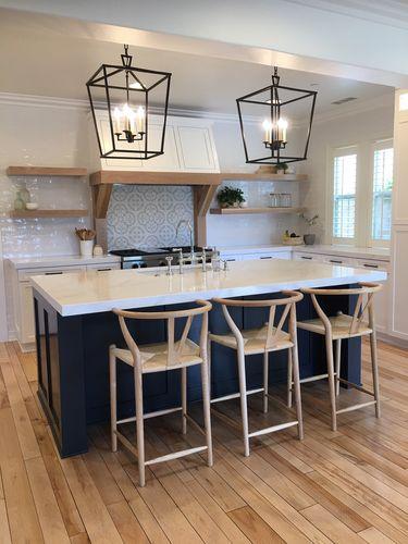 Navy blue island with white countertop and four light wood wishbone bar stools in walnut bar stool style