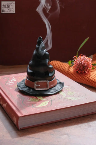 Black ceramic witch’s hat incense cone burner with brown leather belt and silver buckle emitting smoke wisps