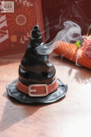 Black witch’s hat incense cone burner with brown belt silver buckle emitting smoke from star-shaped openings