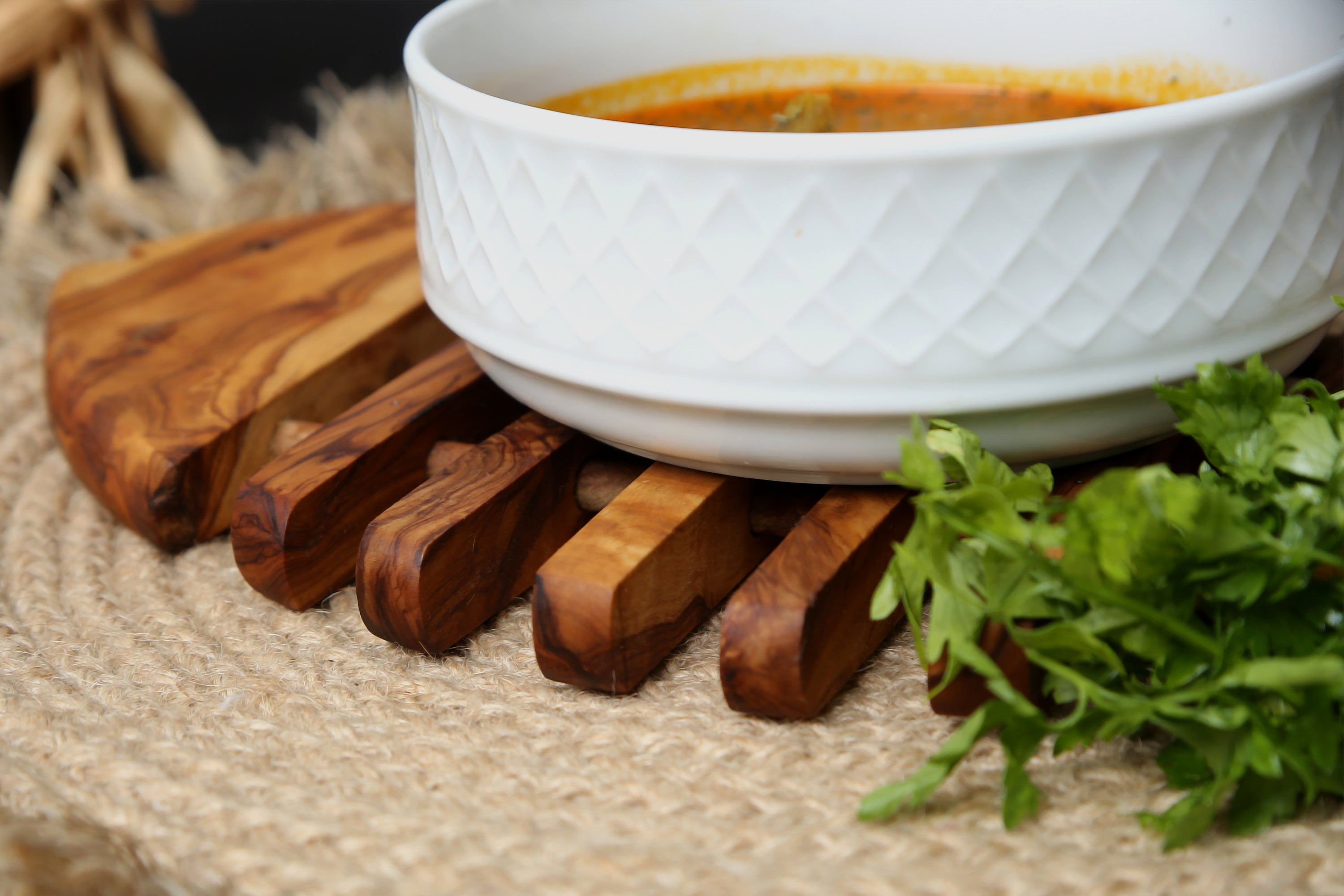 White ceramic bowl with textured diamond pattern next to olive wood fish shaped pan coaster for kitchen use