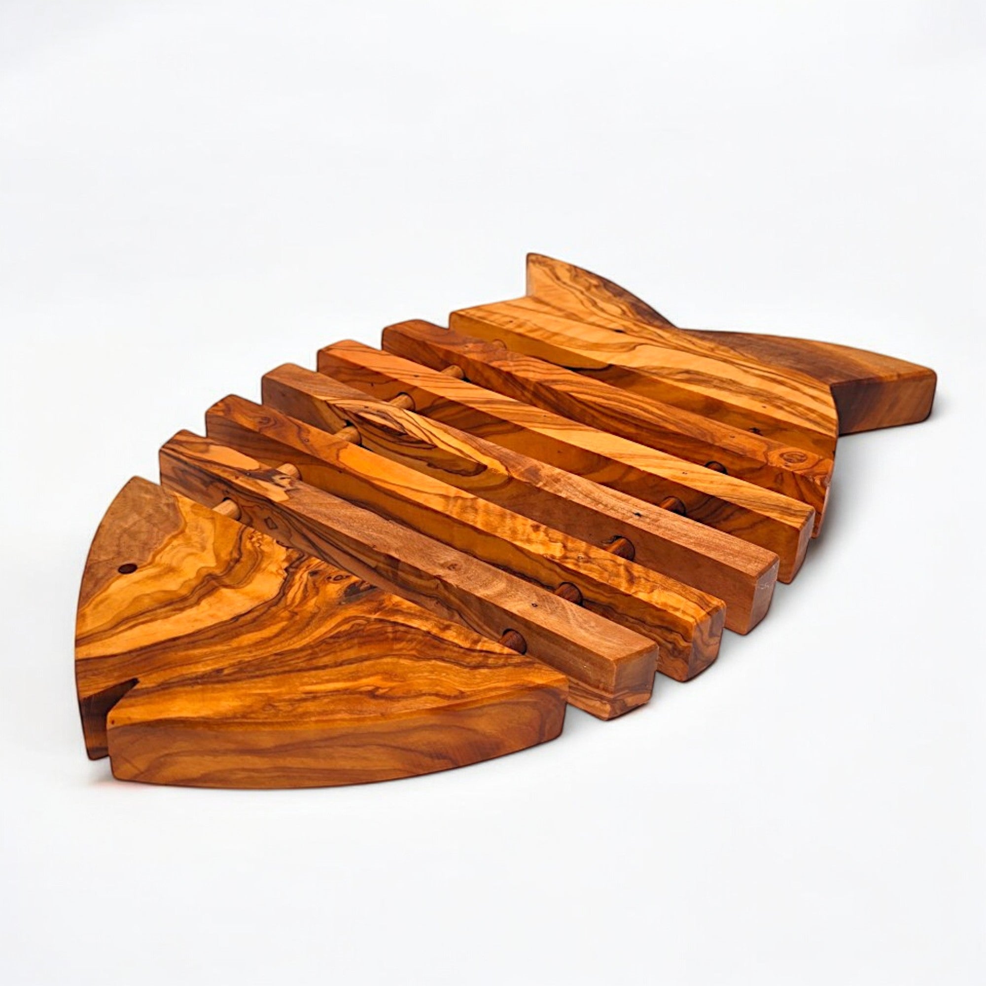 A handmade olive wood fish shaped pan coaster with a warm golden finish and unique swirling grain patterns