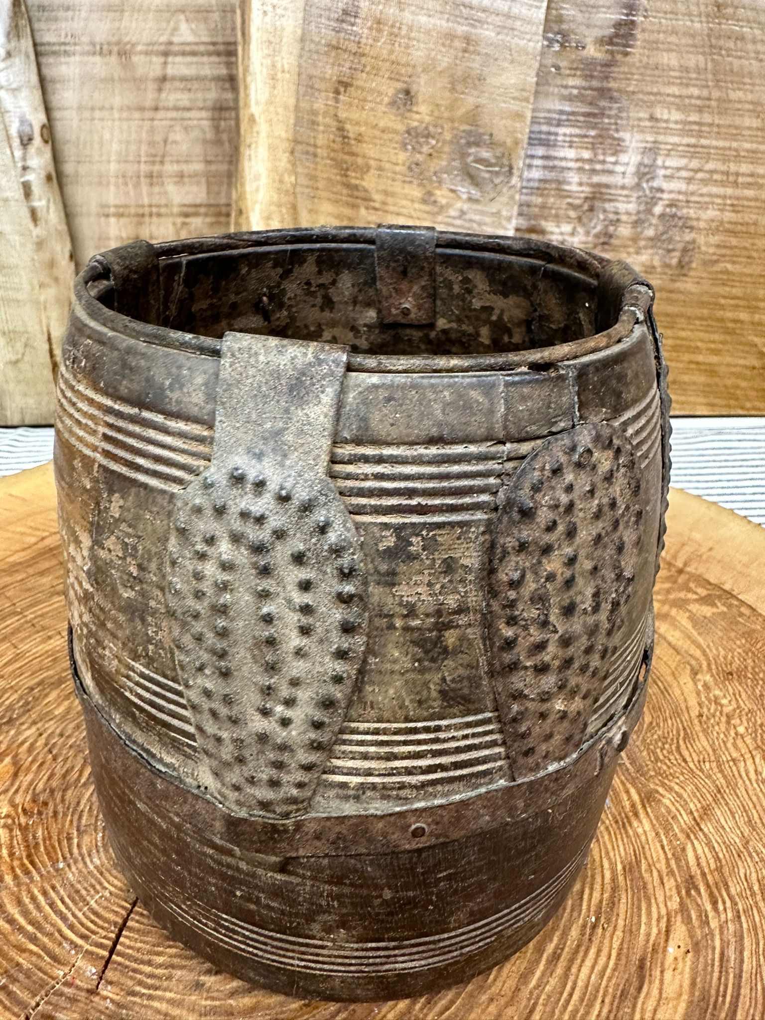 Antique dark metal bucket with embossed patterns and riveted bands used as a wooden vintage herb plant pot and desk tidy