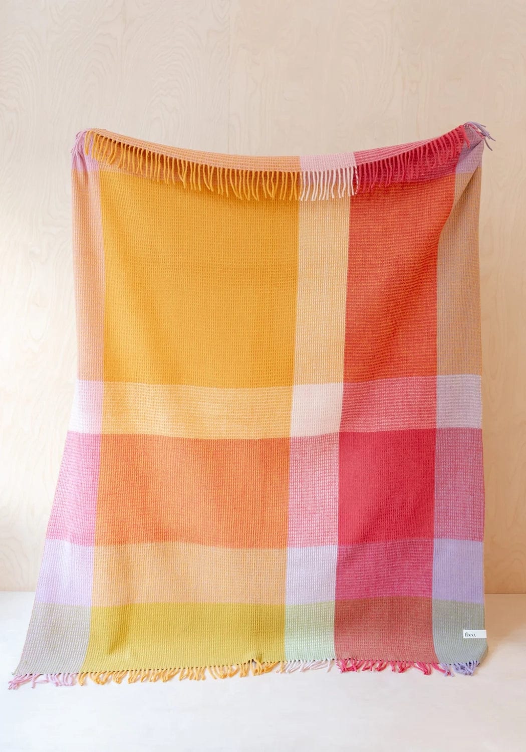 A vibrant wool waffle blanket in orange pink check with soft fringed edges and a textured weave for cozy use