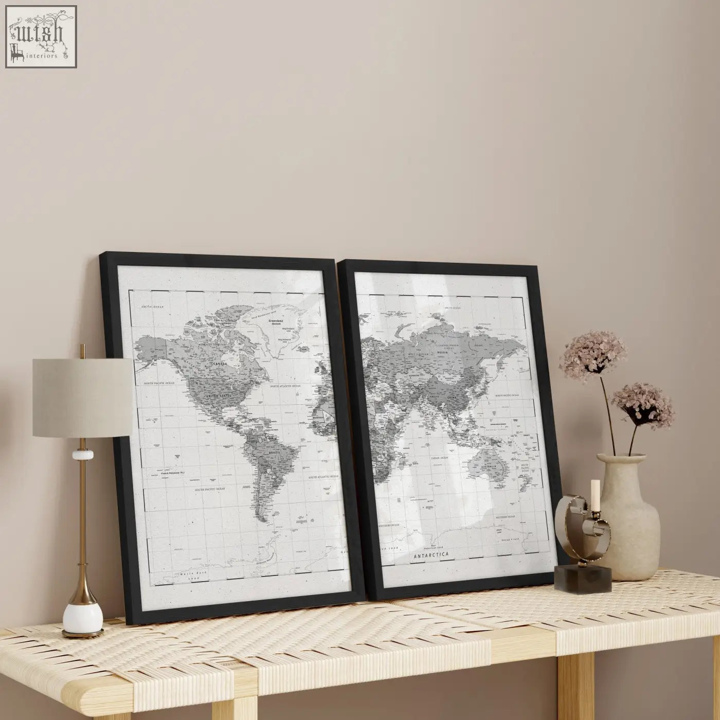 Two black-framed world map prints with detailed grey and white cartography displayed side by side on a woven table