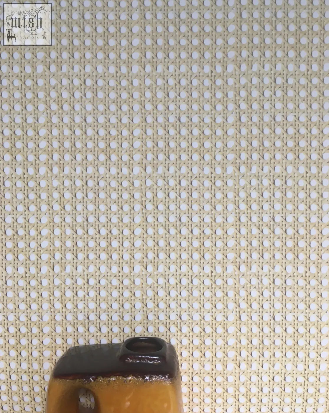 A ceramic vase with glossy amber body and dark brown rim on woven cane wallpaper with textured surface