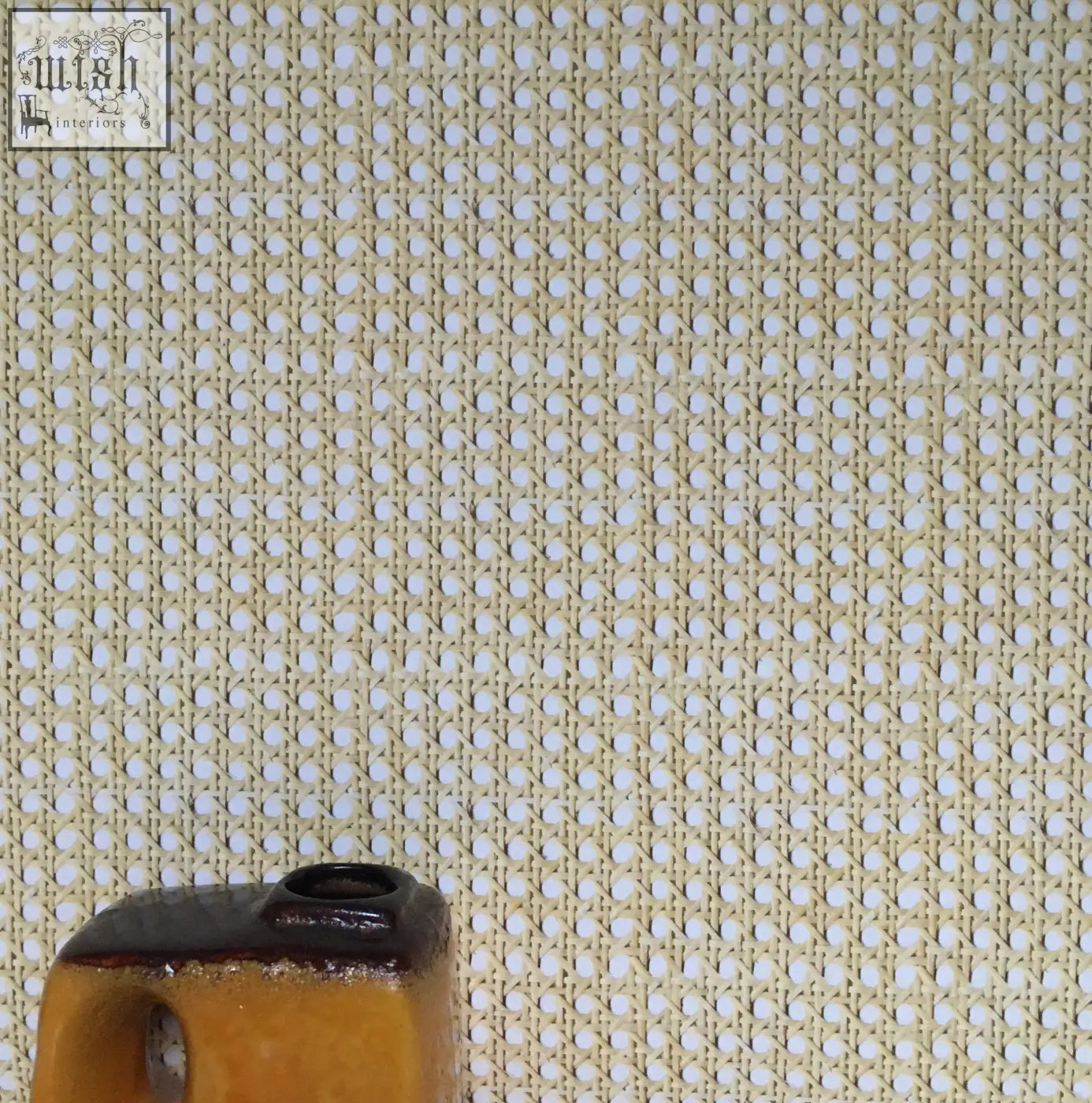 A small mustard yellow ceramic vase with a dark brown rim on a background of woven cane wallpaper texture